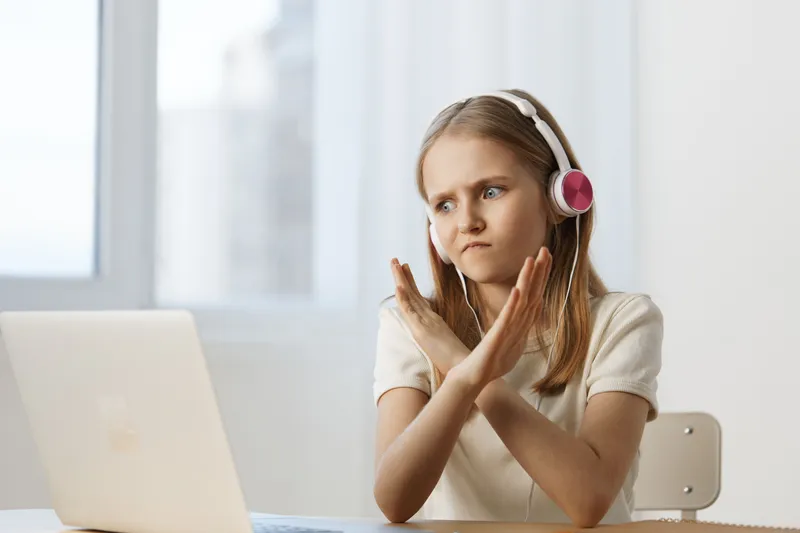 Young girl with headphones expressing frustration while using a laptop, in a bright indoor setting, showcasing emotion and digital interaction