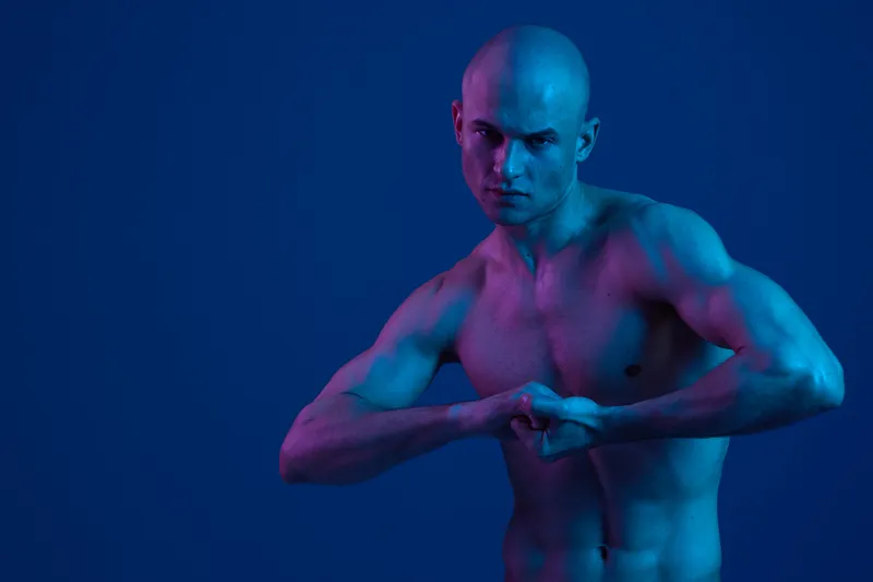 Strong man posing with confidence, showcasing a bold attitude and intense expression. The dramatic lighting emphasizes muscular features and highlights his determination.
