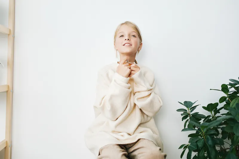 Authentic scene of a cheerful child in a cozy sweater, capturing playful everyday life and simple school moments at home, with soft light and a relaxed, candid mood.