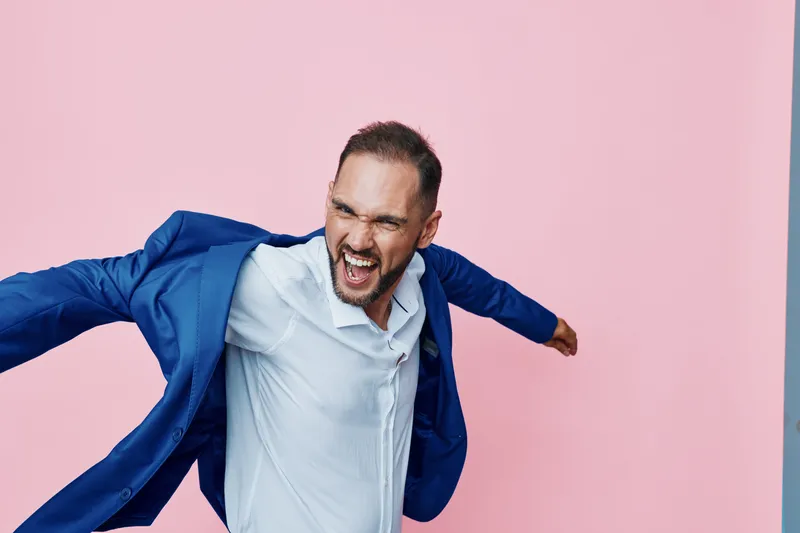 Professional man in a blue suit exudes bold energy against a pink backdrop, portraying ambition and drive. The isolated color background emphasizes a dynamic business mindset and strong emotion for