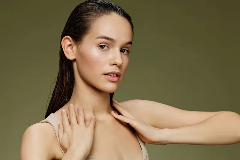 Young woman with natural beauty poses confidently against a soft green background, showcasing healthy skin, minimal makeup, and elegant simplicity