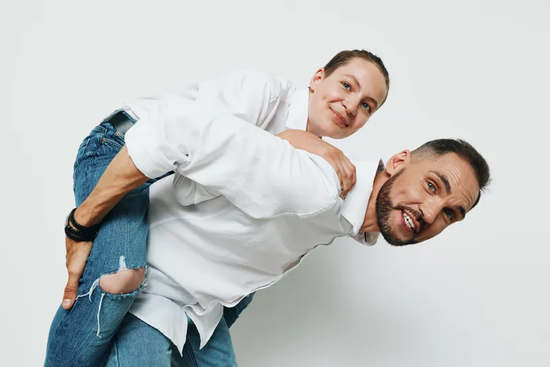 A professional man carries a colleague in a playful pose, showcasing teamwork, confidence, and upbeat energy. An isolated white background emphasizes a strong business mood.
