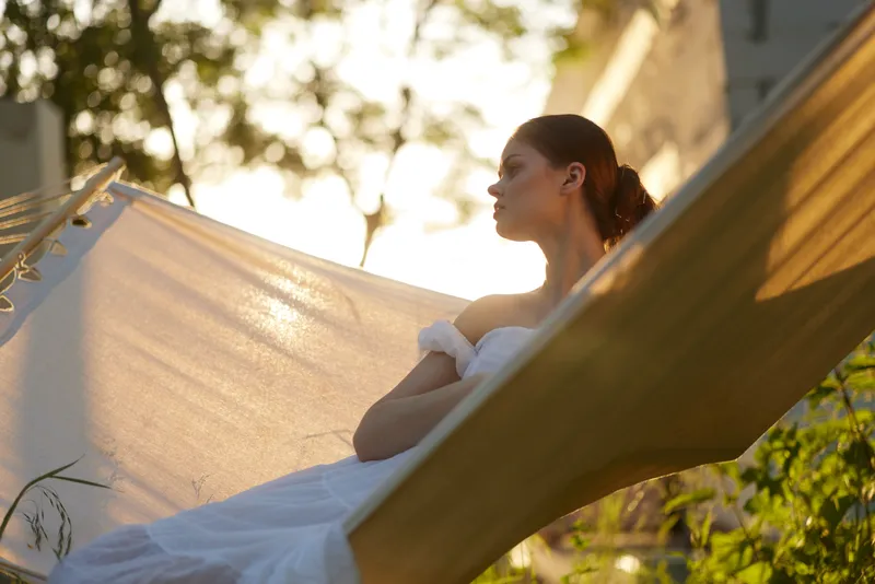 A serene woman in a white dress resting on a hammock at sunset, surrounded by greenery, evoking tranquility and relaxation, perfect for lifestyle and wellness themes