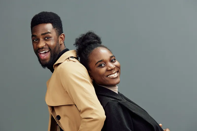 Young happy African couple posing together with joy, showcasing modern fashion styles against a minimalist gray background, perfect for lifestyle and relationships