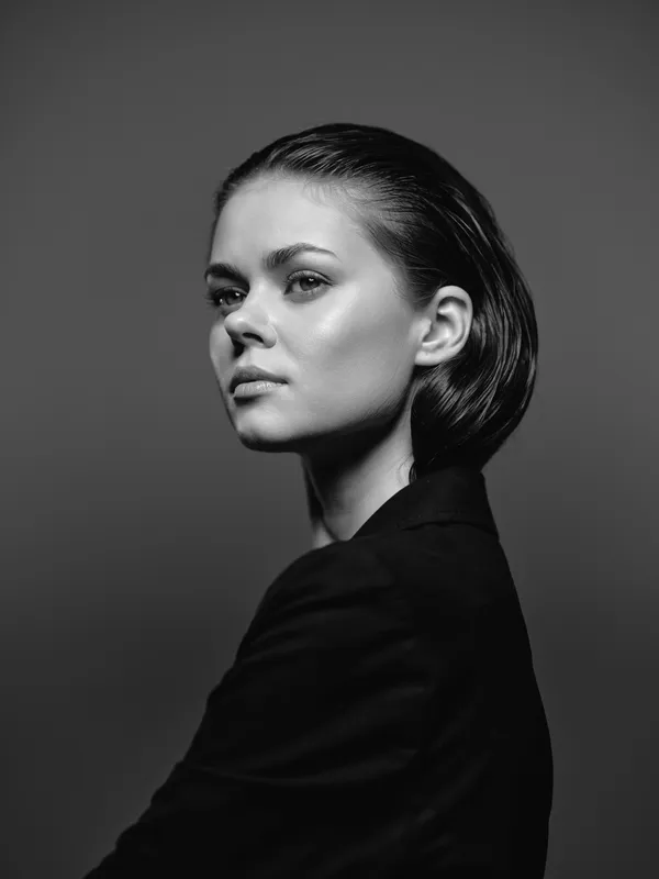 Black and white portrait of a thoughtful woman with short hair and a dark top against a plain background.