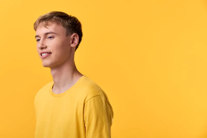 Smiling young man in a bright yellow shirt against a yellow studio backdrop, cheerful expression, casual fashion, positive mood, vibrant lighting and clean composition