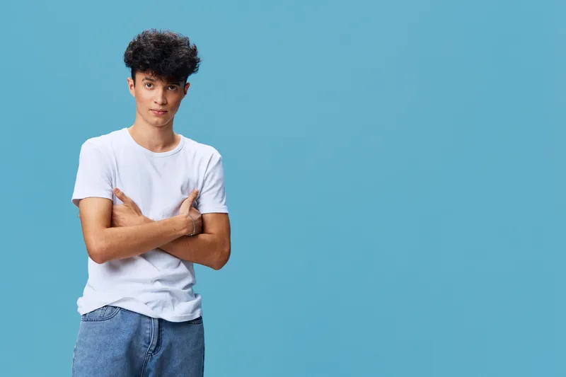young man in white t-shirt with crossed arms standing against blue background, casual style, confident expression, studio portrait, natural lighting
