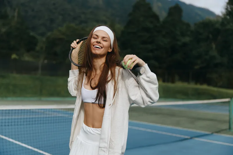 Happy young woman in sporty outfit enjoying tennis on a sunny day, symbolizing fitness, joy, and an active lifestyle with a vibrant background