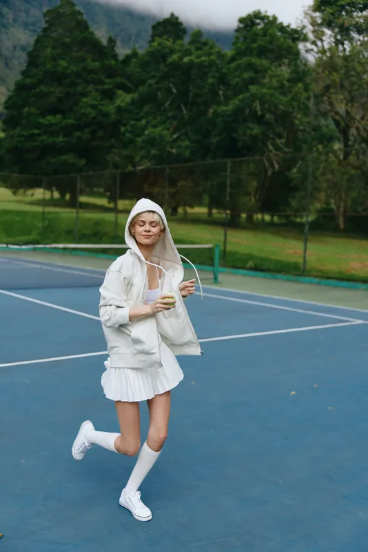 Young woman playing tennis outdoors wearing a stylish white sports outfit, exuding joy and energy on a bright day, perfect for sports enthusiasts and fashion lovers