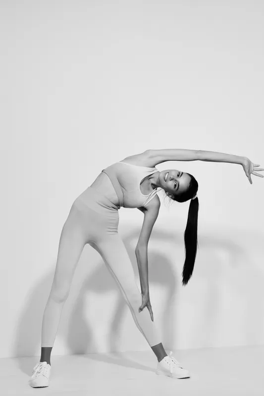 woman sport fitness stretching in monochrome studio, flexible young Asian female athlete wearing activewear performing side bend exercise