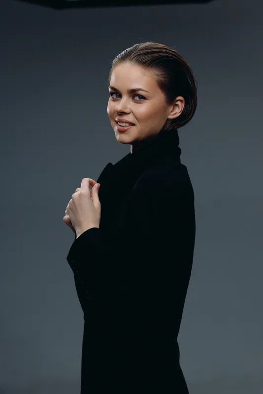 Young smiling woman wearing black turtleneck posing against dark background with confident expression.