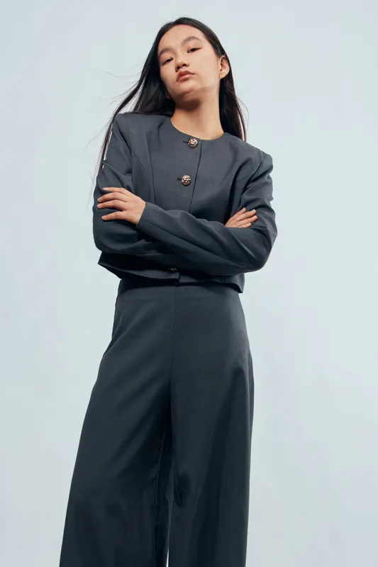 Young woman in dark gray suit with long hair posing confidently with crossed arms against light background. Business fashion outfit, professional look and stylish apparel for office or work.