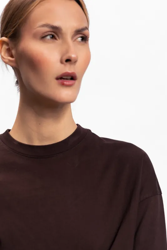 Close-up of a young woman with natural skin wearing a dark brown shirt looking sideways. Studio portrait on white background with soft lighting. Concept of casual fashion and natural beauty.