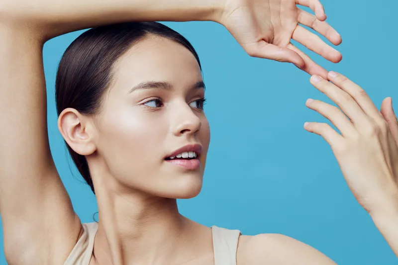Young woman with a natural look posing against a light blue background, showcasing healthy skin and subtle emotions Featuring minimalistic fashion and soft lighting