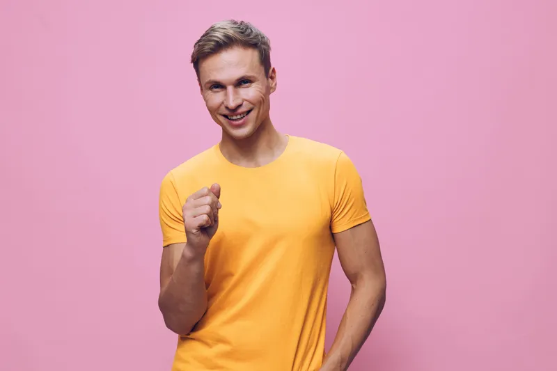 Happy young Caucasian man with short brown hair smiling and pointing at the camera, wearing a yellow t-shirt, casual pose, positive mood, isolated on pink background, studio portrait. Lifestyle concep