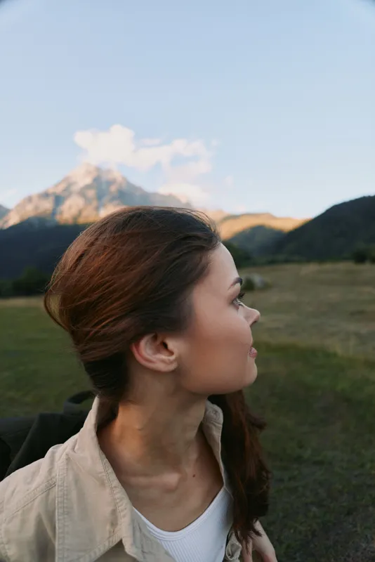 Woman outdoors, profile view, mountain backdrop, sunlit breeze, casual style, natural colors, peaceful lifestyle in expansive landscape with clear sky