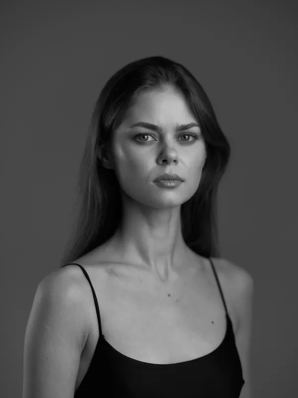 Black and white portrait of a serious woman with long hair wearing a black tank top against a plain background.