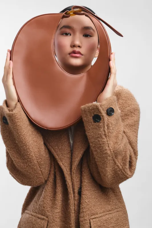 asian woman wears an oversized circular face accessory in a fashion studio, creating a bold yet graceful portrait with muted tones and a mysterious, stylish vibe.