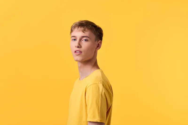 Young man in a yellow tshirt stands in a bright yellow studio backdrop, creating a bold monochrome mood with relaxed posture and a confident gaze