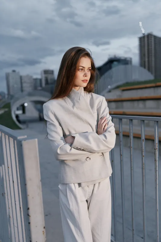 Confident woman in a stylish business suit stands with arms crossed against a modern urban backdrop, exuding professionalism and determination.