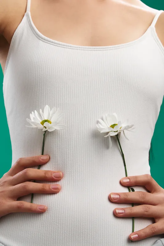 Asian woman wearing a white knit top holds two daisies against a calm, minimal backdrop, creating a gentle, hopeful mood that blends wellness and natural beauty.