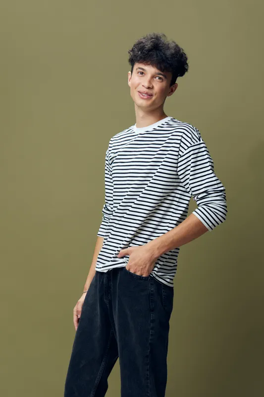 young man in striped shirt posing casually with relaxed smile, dark hair, olive background, casual fashion style, studio portrait with natural light