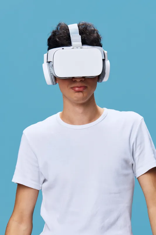 young man wearing virtual reality headset and wireless headphones with white t-shirt, digital technology experience against bright blue background