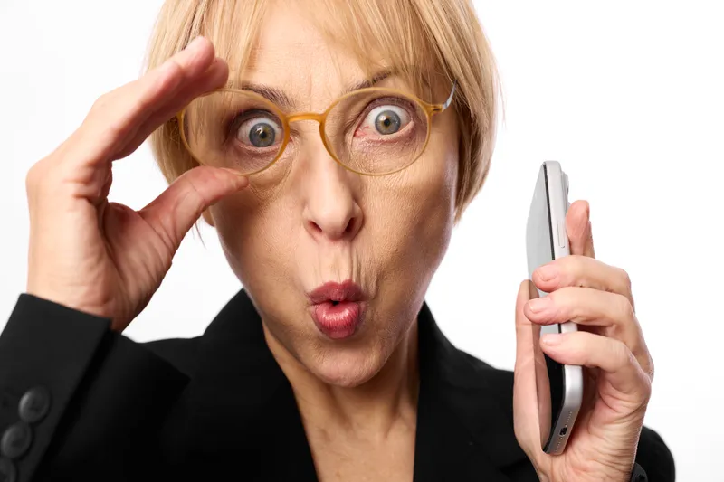 Woman surprised glasses smartphone phone portrait expression communication concept, close up female holding smartphone, hand gesture, shocked face, white studio background, business technology
