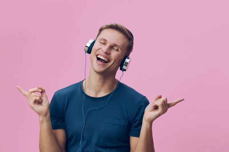 Smiling man enjoying music with headphones on pink background, casual clothing, cheerful mood, youthful, relaxed, lifestyle concept, studio portrait.