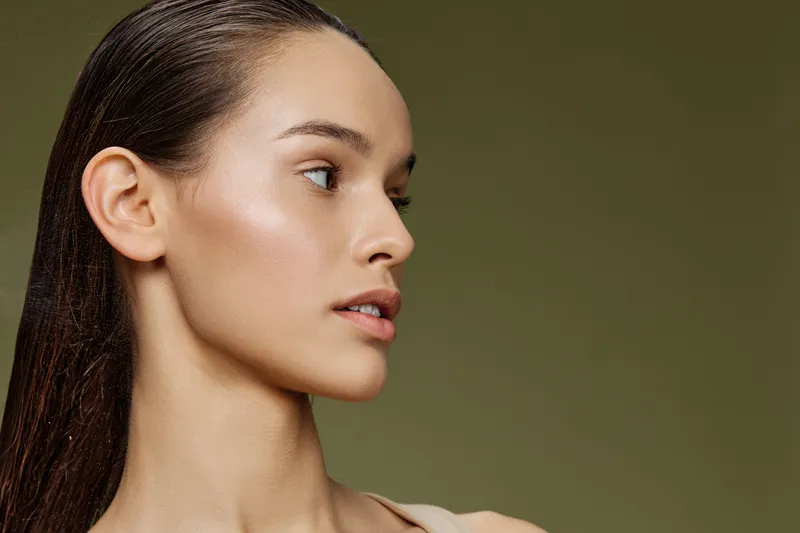 Profile of a young model with glowing skin and long hair, styled in a natural and elegant manner against a soft green background