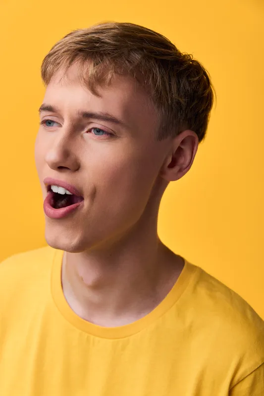 Singing, young man in yellow shirt against bold backdrop, mid performance expression capturing energy and emotion for music, lifestyle, or creative advertising projects