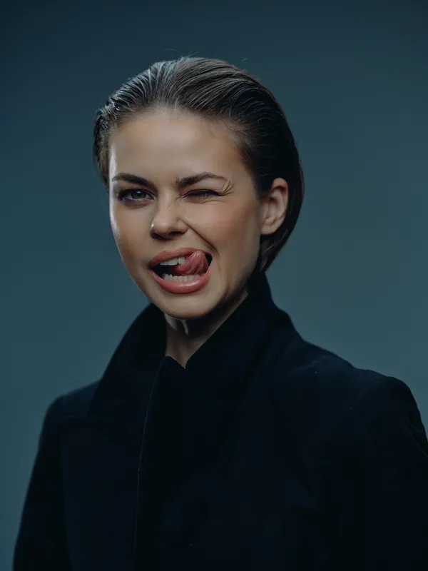 Playful woman winking and sticking out tongue in black jacket with wet hair on dark background