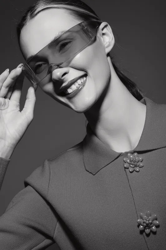 Smiling young white woman with light skin wearing transparent sunglasses and textured top posing in studio. Fashion and beauty concept.