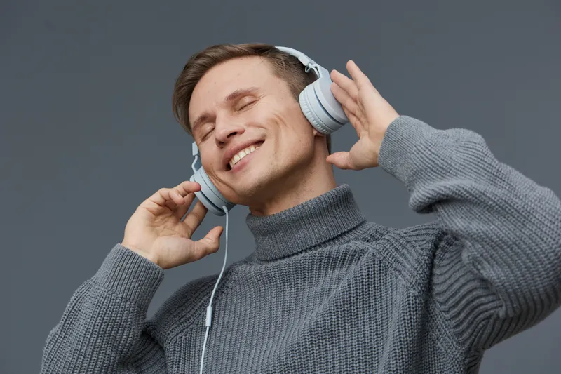 smiling young caucasian man wear grey knitted sweater listen music headphones enjoy relaxation isolated on grey background digital detox mental health concept