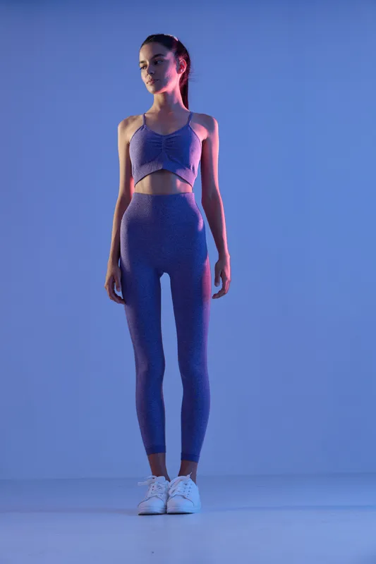 Sport fitness woman in stylish activewear standing in blue studio light, showcasing toned body and athletic posture for health and workout concept.