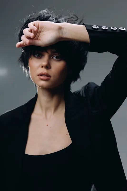 young woman in black blazer with short dark hair posing indoors in moody lighting