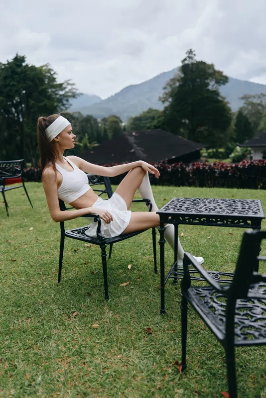 Fit young woman in white sports attire relaxing on a chair in lush greenery, showcasing confidence and a healthy lifestyle