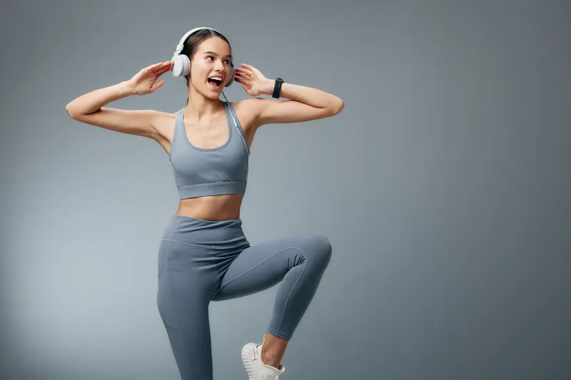 Woman in athletic wear with headphones performs energetic workout poses in a studio, showcasing fitness, sport and active lifestyle in a dynamic motion scene.