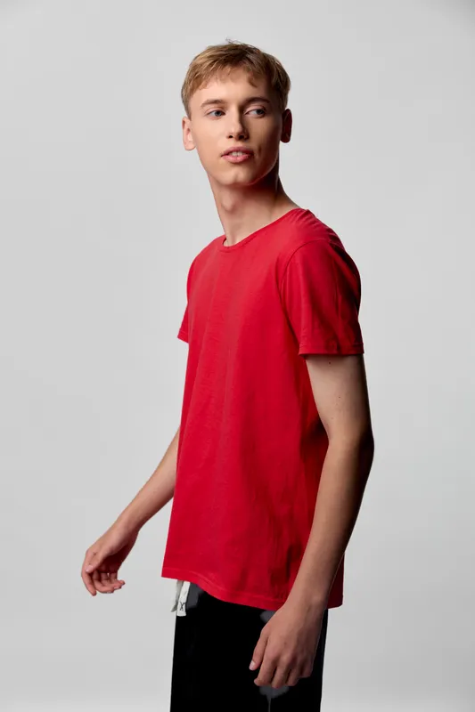 Young man in a red t shirt stands in a neutral studio, casual fashion with clean lighting, relaxed pose, minimalist backdrop, ideal for lifestyle, fashion catalogs and advertising.