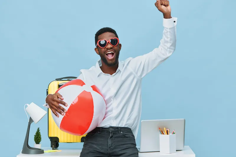 Cheerful young man with sunglasses holding beach ball in bright office setting, celebrating vacation mood, casual style, summer vibes, happy expression, travel concept, lifestyle photography.