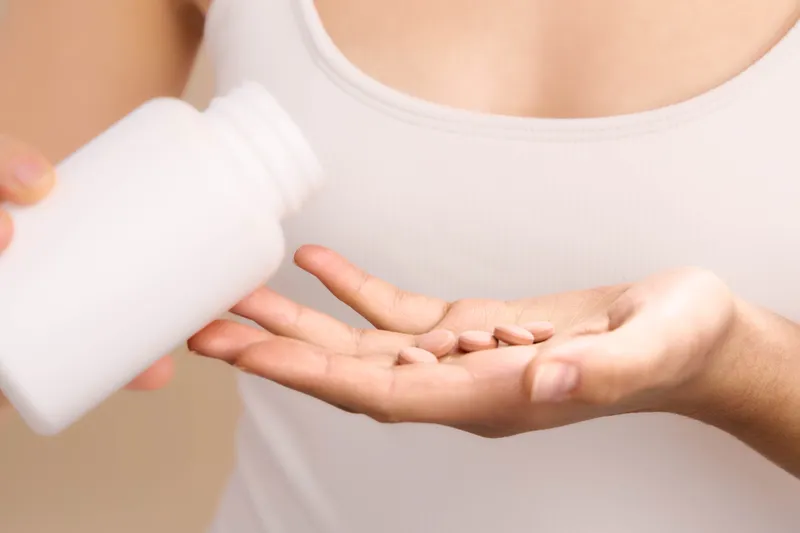 Asian woman applies lotion from a bottle onto her palm in a minimal studio setting, conveying care and wellness. The scene shows a calm, mindful self care moment in a modern lifestyle.