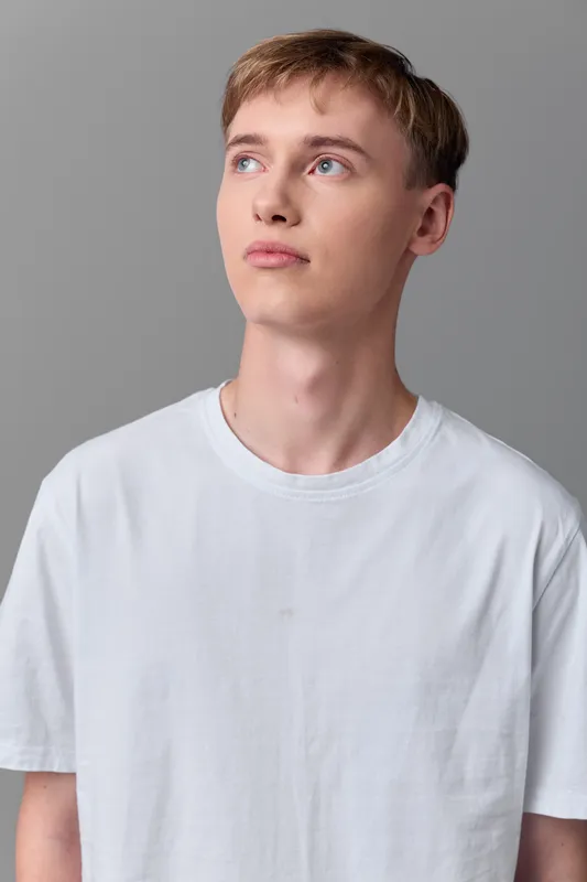 Young man looking up in a white t shirt against a neutral studio background, casual style and thoughtful expression in a clean, minimal setting