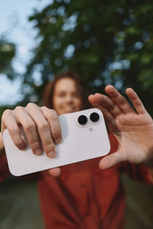 Cheerful woman outdoors, taking a selfie with smartphone, bright daylight, soft background blur, casual outfit, relaxed mood, natural colors, candid moment, joyful atmosphere, fresh air