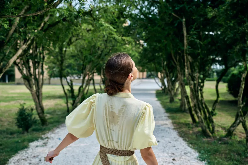 Woman dress park path trees walking, back view of woman in pale yellow dress walking on gravel path through green tree tunnel, outdoor authenticity inclusivity