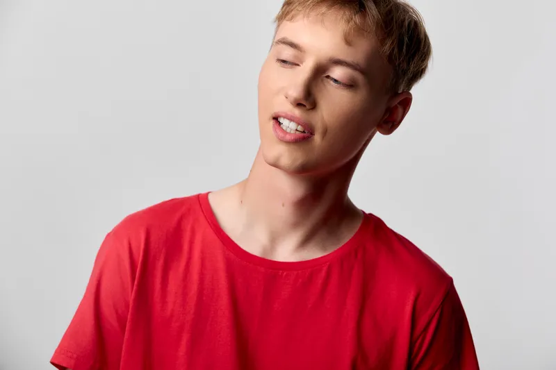 Man, relaxed mood with closed eyes wearing a red shirt in a simple studio setting, conveying calm, casual style and comfort for lifestyle, wellness and everyday moments