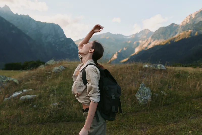 Young woman with backpack enjoying fresh air in mountain landscape. Outdoor lifestyle concept with natural light and scenic background of rocky hills and sky.