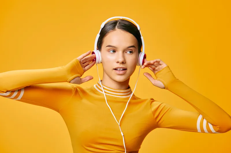 Fitness-minded woman in a vivid orange studio, wearing a long-sleeve top and headphones, posing during a workout with energetic vibe and focus.