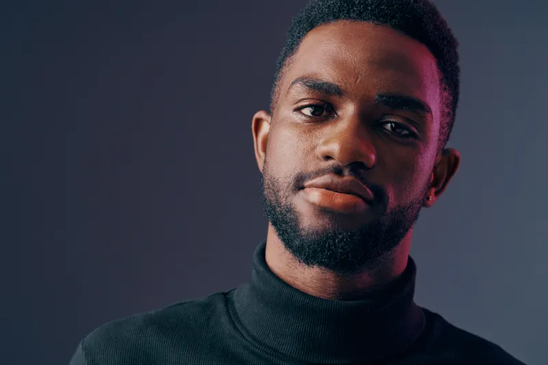 Portrait of a confident Black man in a black turtleneck, displaying a serious expression against a dark gradient background, ideal for themes of empowerment and style