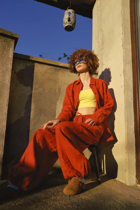 A confident woman wearing a red blazer and yellow crop top sits on a chair outdoors, capturing bold color, street style, and relaxed attitude in warm sunlight