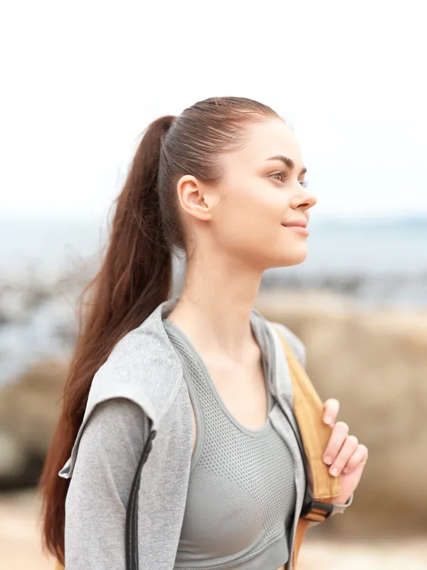 Young woman in athletic wear enjoying a healthy lifestyle by the beach, radiating positivity and confidence in a serene environment
